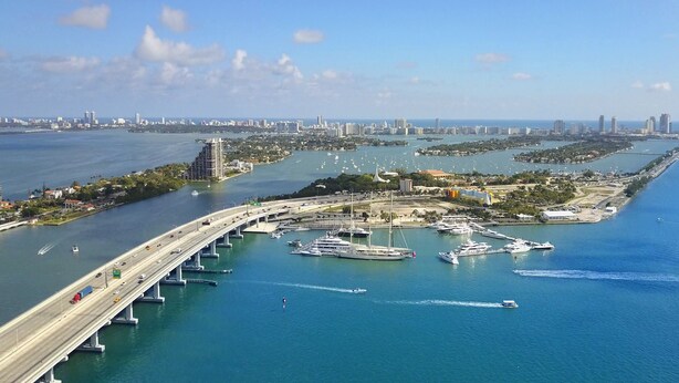 An aerial view of a coastal city with a prominent bridge, marina, and urban skyline. - OCEAN DRIVE APARTMENTS (Miami Beach)