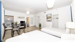 A modern hotel room with a bed, a desk with a chair, a television, and a dining area with chairs and a table. - OCEAN DRIVE APARTMENTS (Miami Beach)