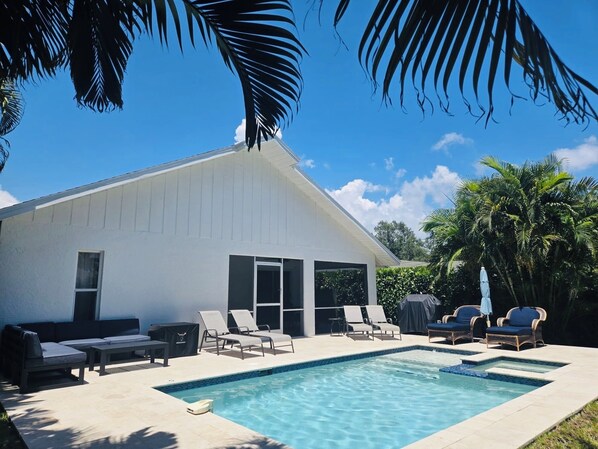 A modern house with a swimming pool, lounge chairs, and a covered patio area.