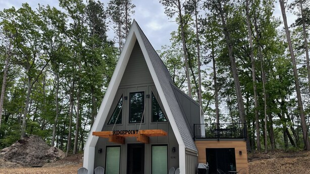 A modern A-frame cabin with a covered porch, two chairs, and a small table. - Ridge Point | Walk to Glen Arbor | Pet-Friendly | Close to Sleeping Bear Dunes (Glen Arbor)