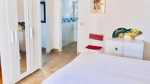 A bedroom with a bed, a white wardrobe, a red chair, a small table with decorative fans, and a painting on the wall. - Blue Med Smurf, Palinuro, Cilento (Palinuro)