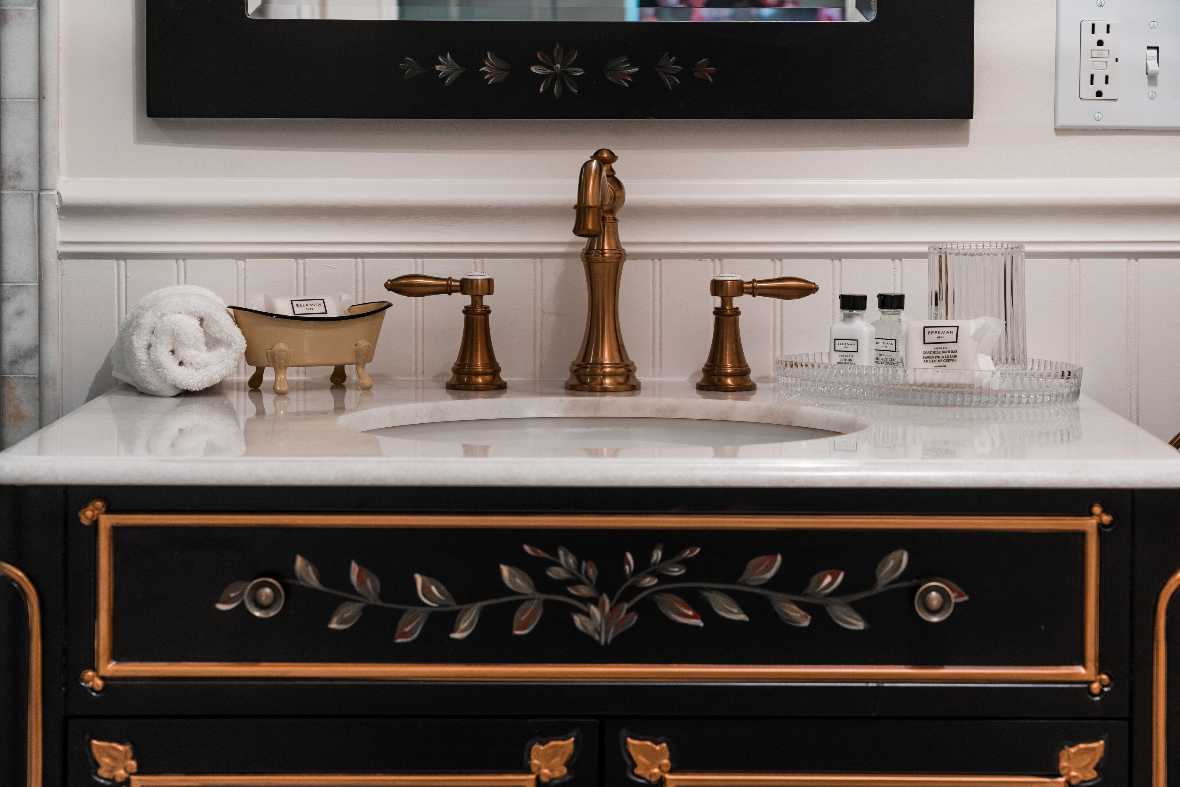 A bathroom vanity with a white marble countertop, a black and gold cabinet, and a brass faucet.