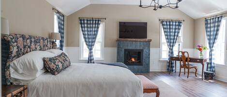 A spacious bedroom with a large bed, a fireplace, a desk, and a chair.