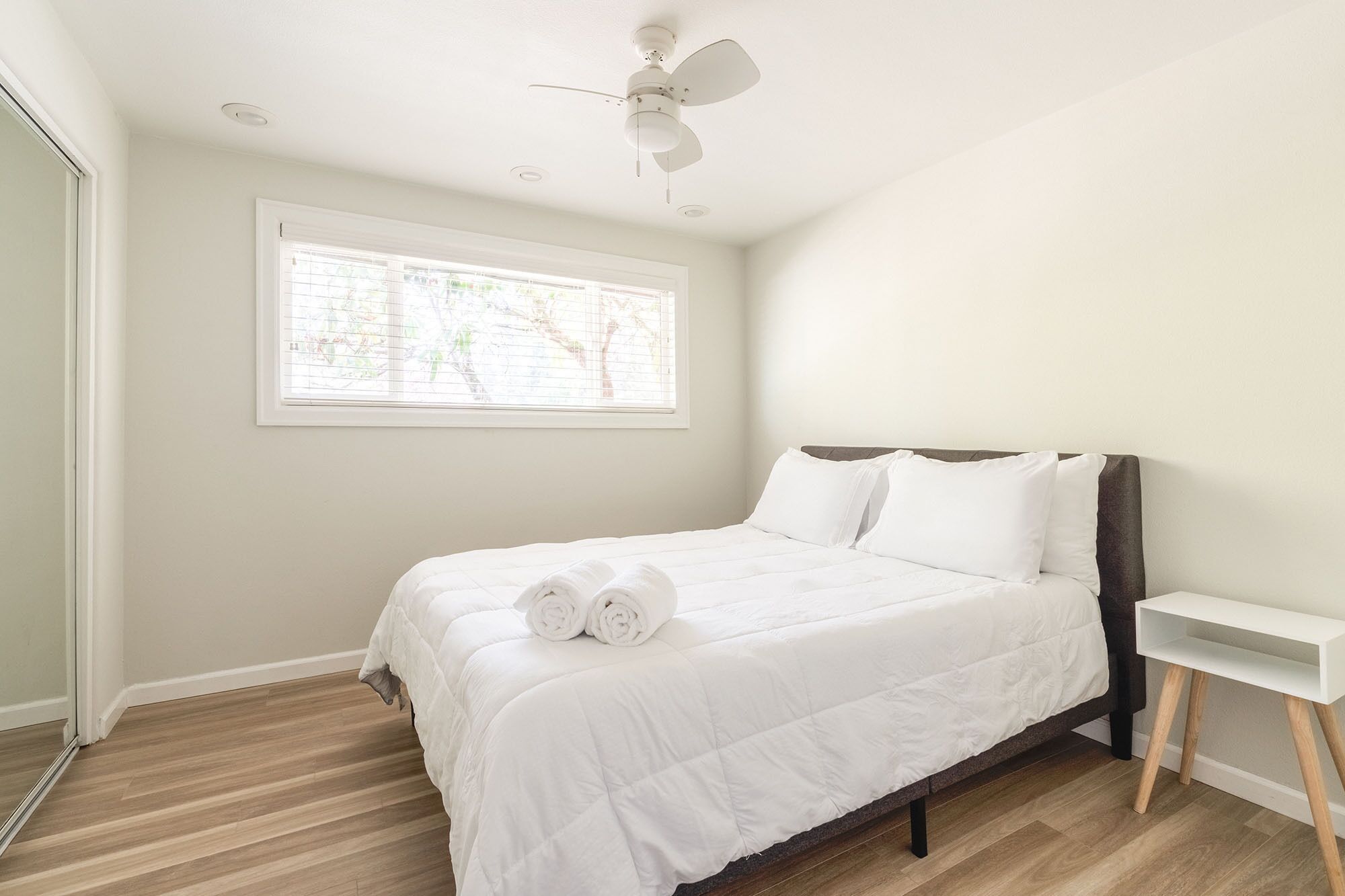 Un dormitorio con cama, ventilador de techo, ventana y mesita de noche.