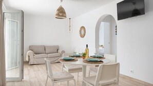 Una sala de estar moderna con un sofá, una mesa de comedor, sillas, un televisor y un espejo grande.