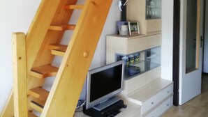 Un escalier en bois mène à une mezzanine où se trouve un téléviseur posé sur un meuble blanc.