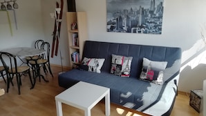 Un salon avec un canapé bleu foncé, une table basse blanche et un tableau représentant un paysage urbain accroché au mur.