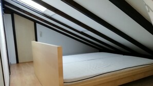 Une petite chambre avec un lit simple, un plafond en pente, un plancher en bois et un cadre de lit sobre.