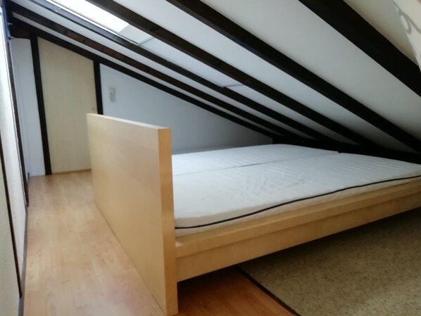 Una habitación pequeña con cama individual, techo inclinado, suelo de madera y estructura de cama sencilla.