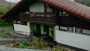 Une maison à deux étages, dotée d’un toit en pente, d’un balcon et d’un petit jardin agrémenté de rochers et de plantes.
