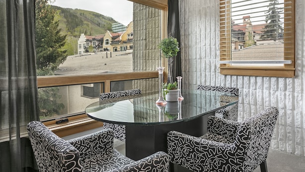 A dining area with a glass table and patterned chairs, a potted plant, and a view of a town and hills. - Lionshead Village Condo, Perfect Location 100 Yards from Slopes, Hot Tub! (Vail)