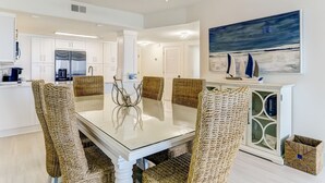 A modern kitchen with white cabinets, stainless steel appliances, and a glass dining table surrounded by woven chairs. - RARE Direct Oceanfront Condo with TWO private balconies within OMNI resort (Fernandina Beach)