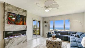 A modern living room with a fireplace, a large abstract painting, a blue sofa, and a view of the ocean. - RARE Direct Oceanfront Condo with TWO private balconies within OMNI resort (Fernandina Beach)
