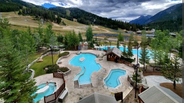 Un complexe hôtelier doté de plusieurs piscines, d’un chalet en bois et offrant une vue sur un paysage montagneux.