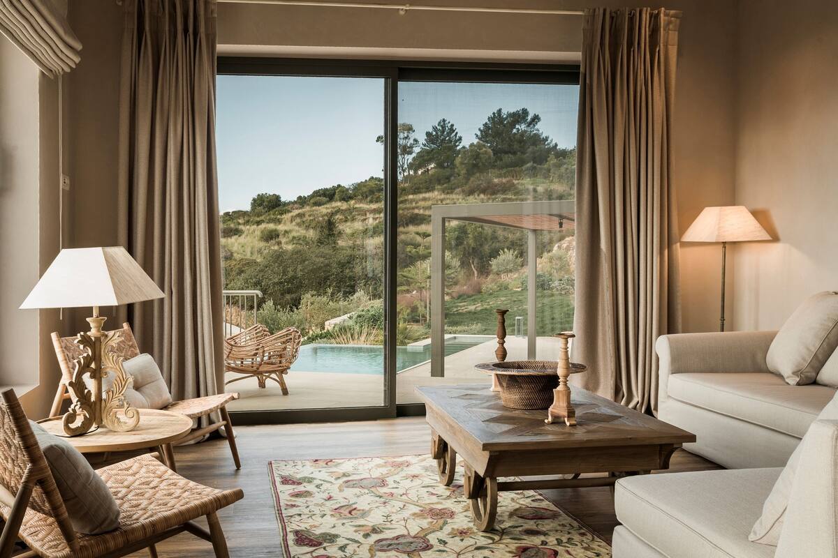 Ein geräumiges Wohnzimmer mit einer großen Glasschiebetür, die zu einem Pool führt, mit Korbmöbeln und einem Holztisch.