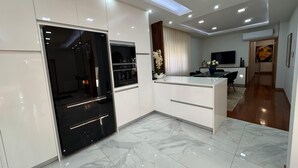 A modern kitchen with a built-in oven and microwave, a dining area with a table and chairs, and a living room with a flat-screen TV.