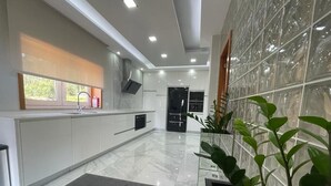 A modern kitchen with white cabinets, a grey rug, and a large window.