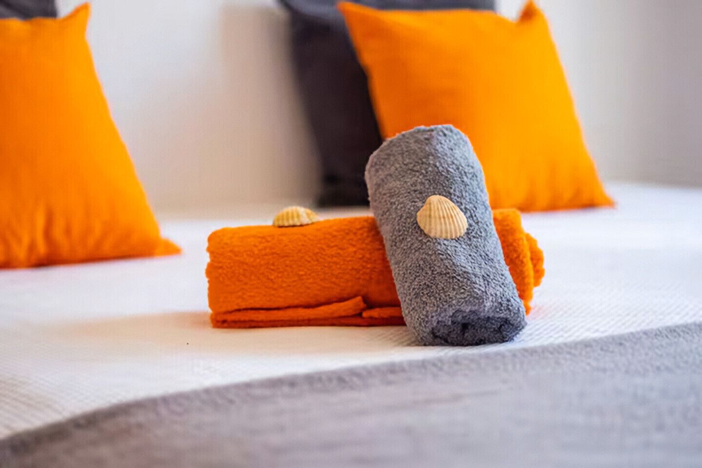 A bed with two towels, one orange and one grey, and a seashell on the grey towel.