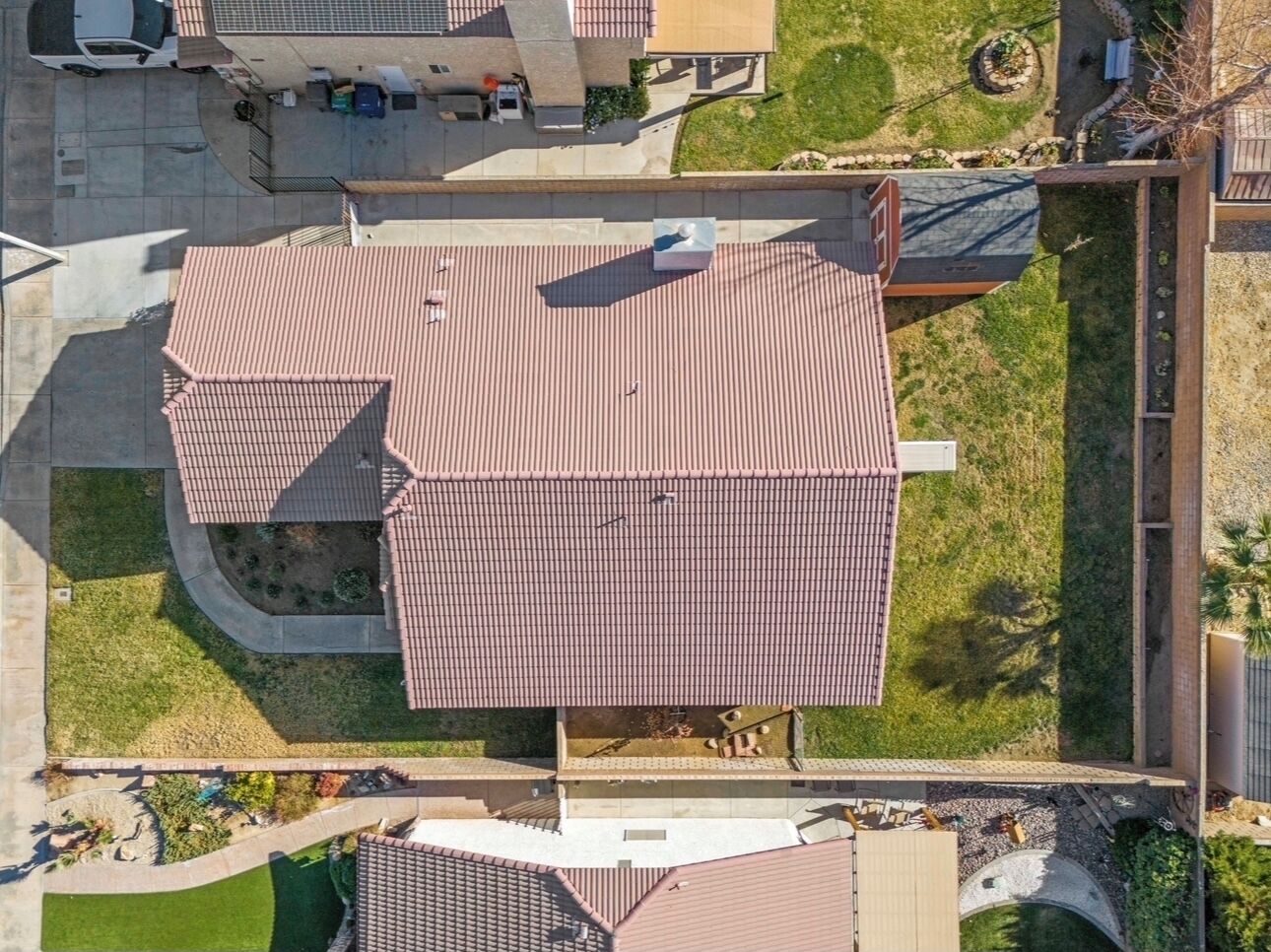An aerial view of a residential area with a prominent house featuring a red-tiled roof, a driveway, and a well-maintained lawn.