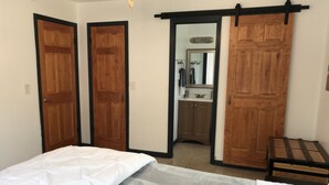 Un dormitorio con cama, armario y baño visible a través de una puerta abierta.