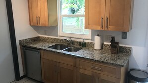 Una cocina con encimeras de granito, armarios de madera, un fregadero de acero inoxidable y una ventana con vistas al verdor.