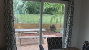 Una habitación con un amplio ventanal corredera que da a un patio exterior con un banco y sillas de madera.