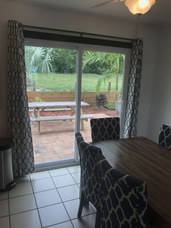 A room with a large sliding glass door leading to an outdoor patio with a wooden bench and chairs.