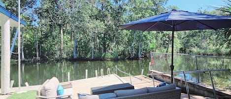 A dock with outdoor furniture, a covered area, and a view of a lake surrounded by trees.