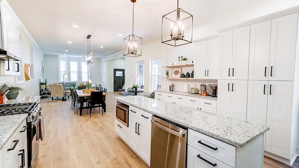 A modern kitchen with white cabinets, granite countertops, and stainless steel appliances. There are pendant lights above the island and a dining area with a table and chairs. - Modern Luxury Home: 7 Mins From Downtown-Sleeps 12 (Cincinnati)