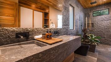 Un baño moderno con pared de piedra, techo de madera y un espejo grande.