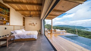 A modern bedroom with a large bed, wooden flooring, and a view of a lush landscape. - LALOON Luxury Suites - Adults Only (Cóbano)