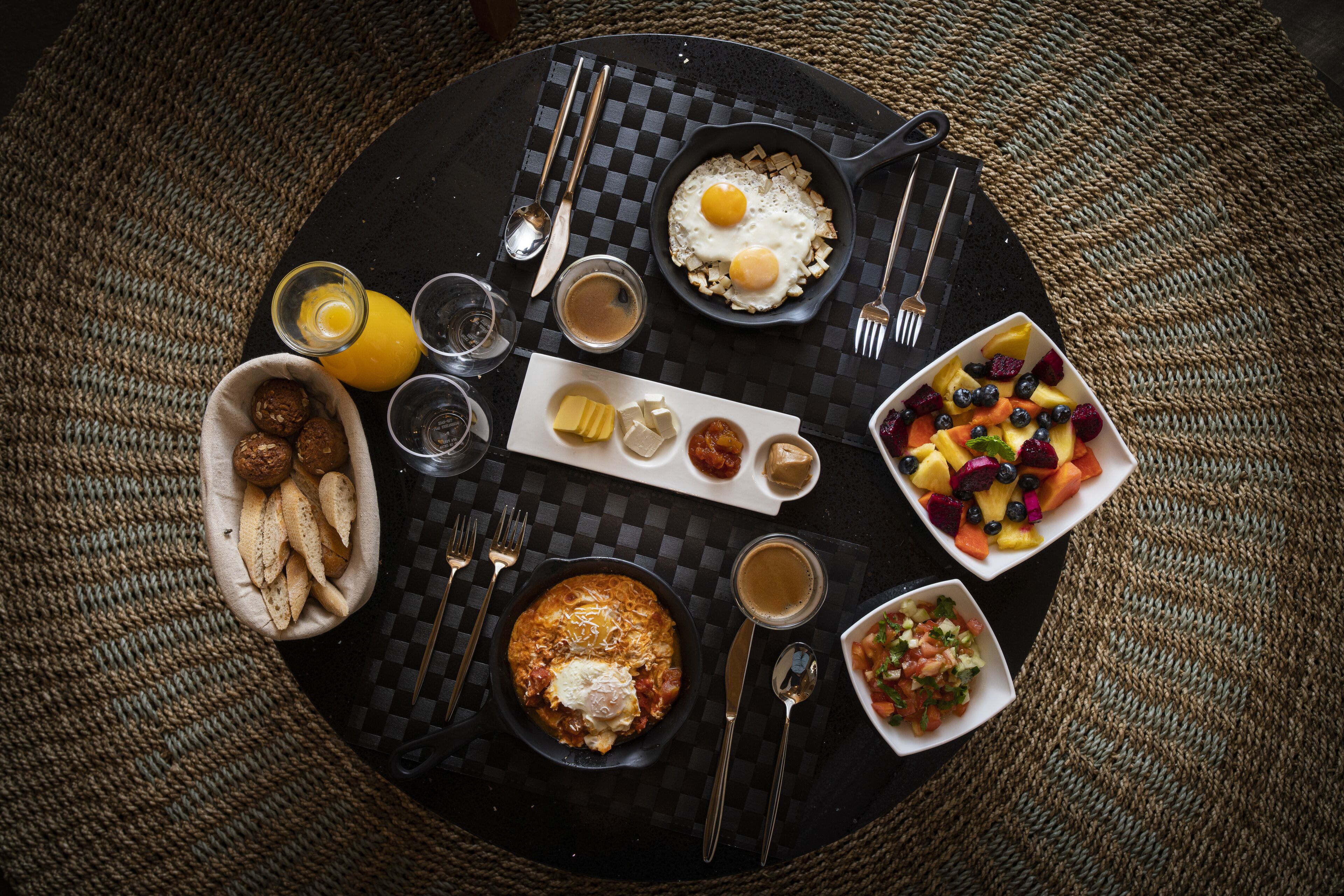 A breakfast setting with a variety of food items including eggs, toast, fruit, and beverages on a checkered table.