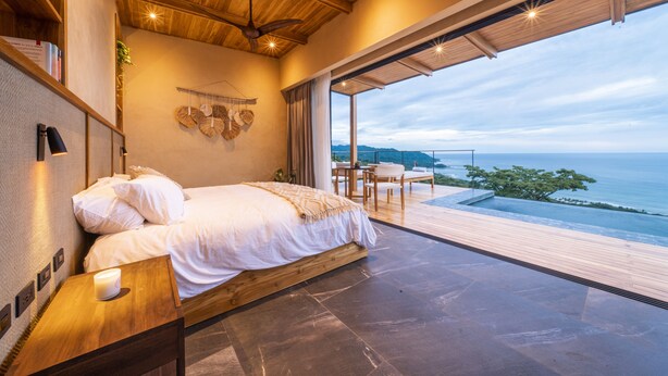 A bedroom with a bed, a nightstand, a desk, and a view of the ocean. - LALOON Luxury Suites - Adults Only (Cóbano)
