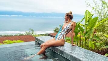A woman sitting on a pool edge with a view of the ocean.