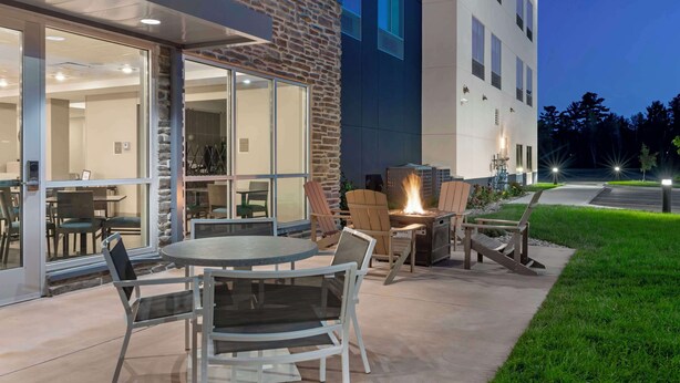 An outdoor patio area with a round table and chairs, a fire pit, and a view of the building's interior through glass doors. - Best Western Plus Grand Rapids MN (Grand Rapids)