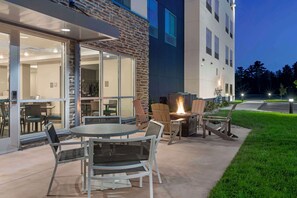 An outdoor patio area with a round table and chairs, a fire pit, and a view of the building's interior through glass doors. - Best Western Plus Grand Rapids MN (Grand Rapids)