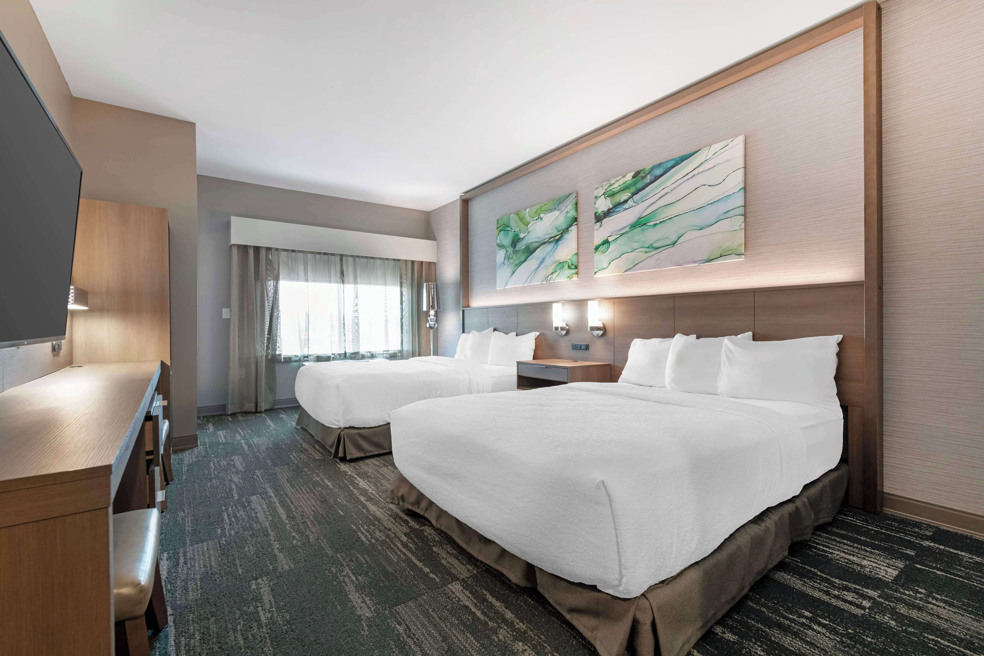 A hotel room with two beds, a desk, and a large window with curtains.