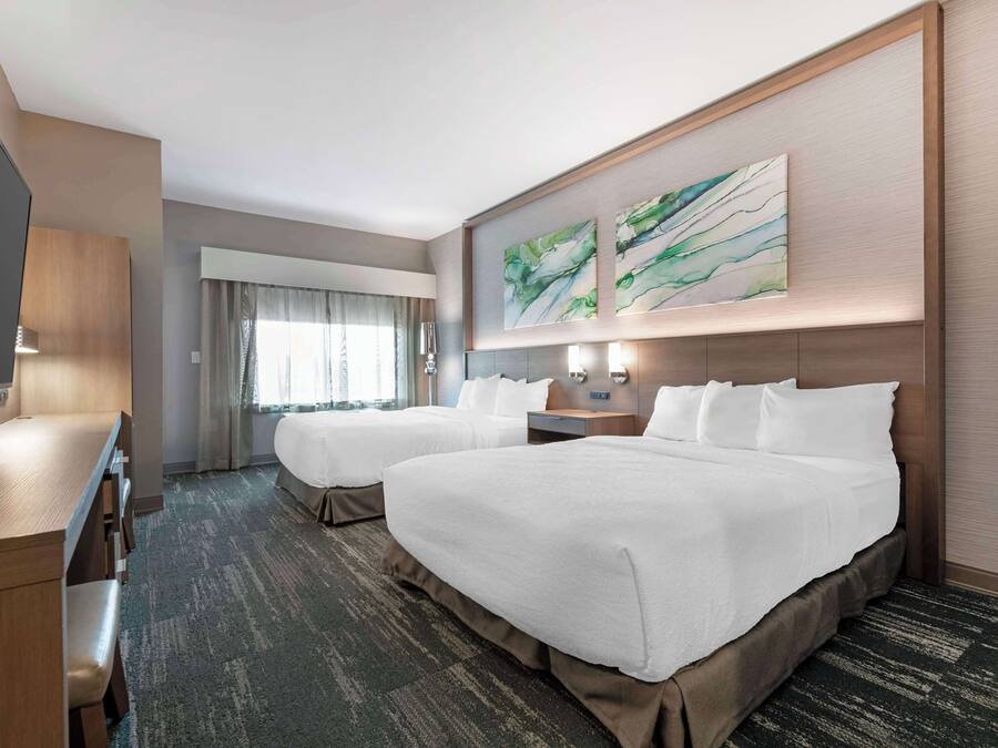 A hotel room with two beds, a desk, and a large window with curtains.