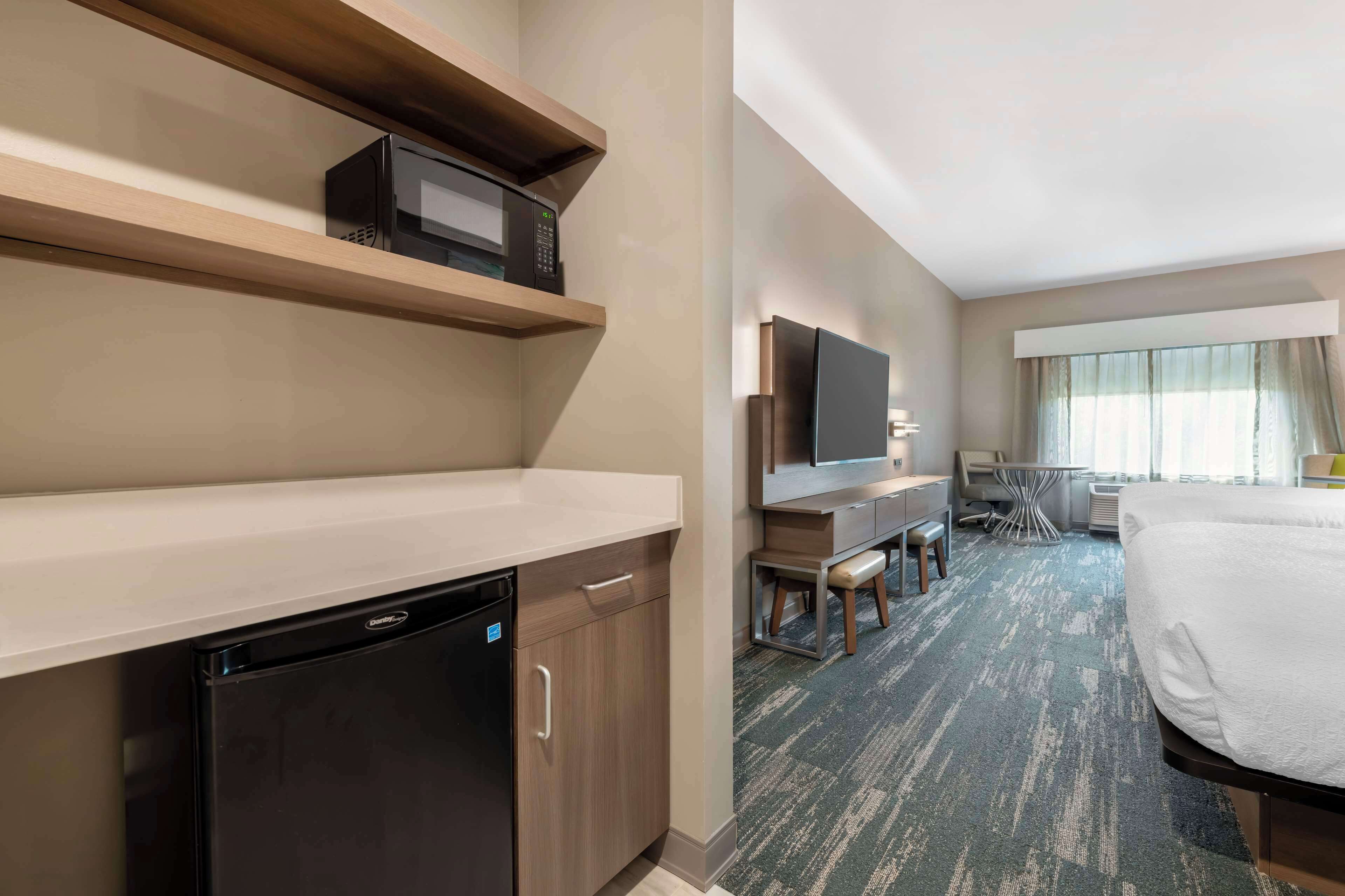 A hotel room with a kitchenette, a bed, a TV, and a desk with a chair.
