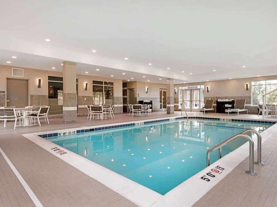 An indoor swimming pool with clear water, surrounded by lounge chairs and tables, and a ceiling with recessed lighting.