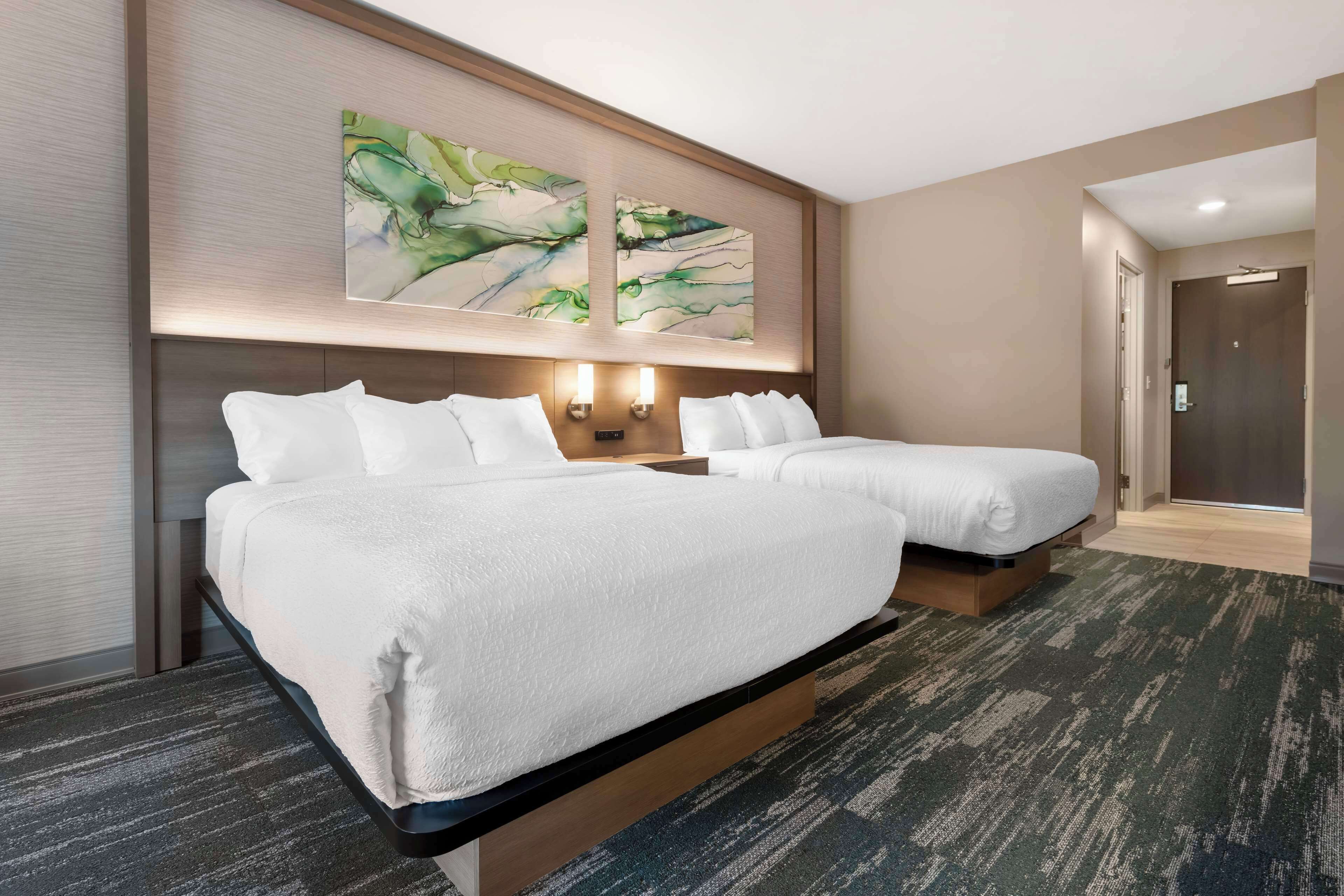Habitación de hotel con dos camas, un cuadro abstracto grande sobre la cabecera y suelo alfombrado.