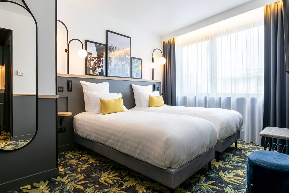 Habitación de hotel con dos camas, un ventanal con cortinas, una mesita y un espejo.