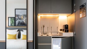 A compact hotel room with a bed, a small kitchenette, and a view of a cityscape.