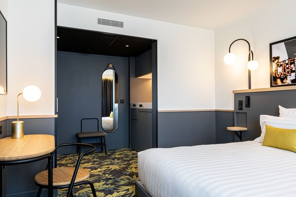 Una habitación de hotel con una cama, un escritorio, una silla, un espejo y una mesita.