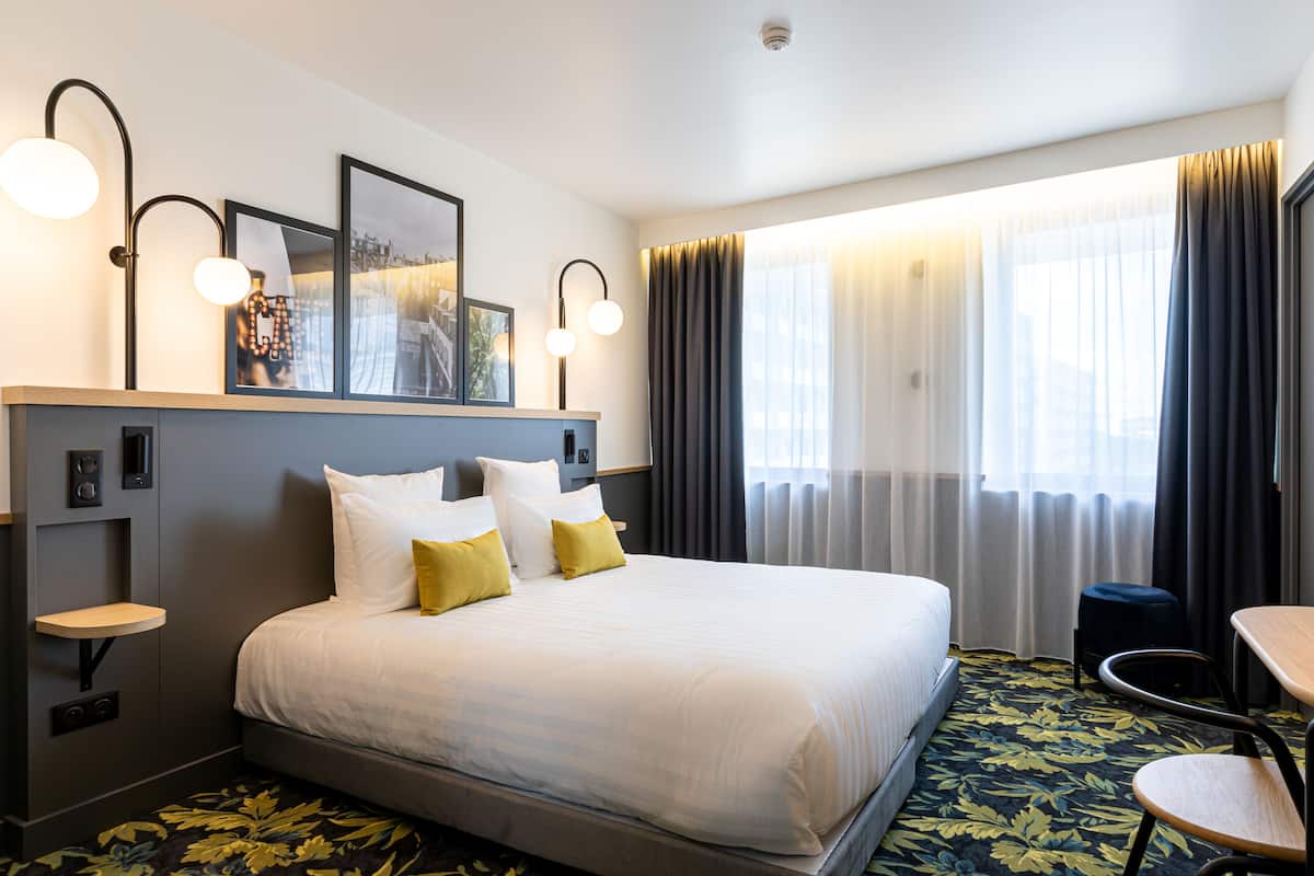 Una habitación de hotel con una cama grande, mesitas de noche, un escritorio y una silla.