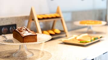 Een buffet met diverse gerechten, waaronder een stuk taart op een glazen standaard, een fruitschaal en een dienblad met belegde broodjes.