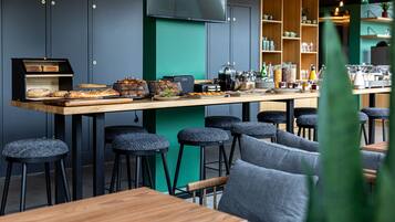 A modern café with a long counter, stools, and a variety of food items displayed.