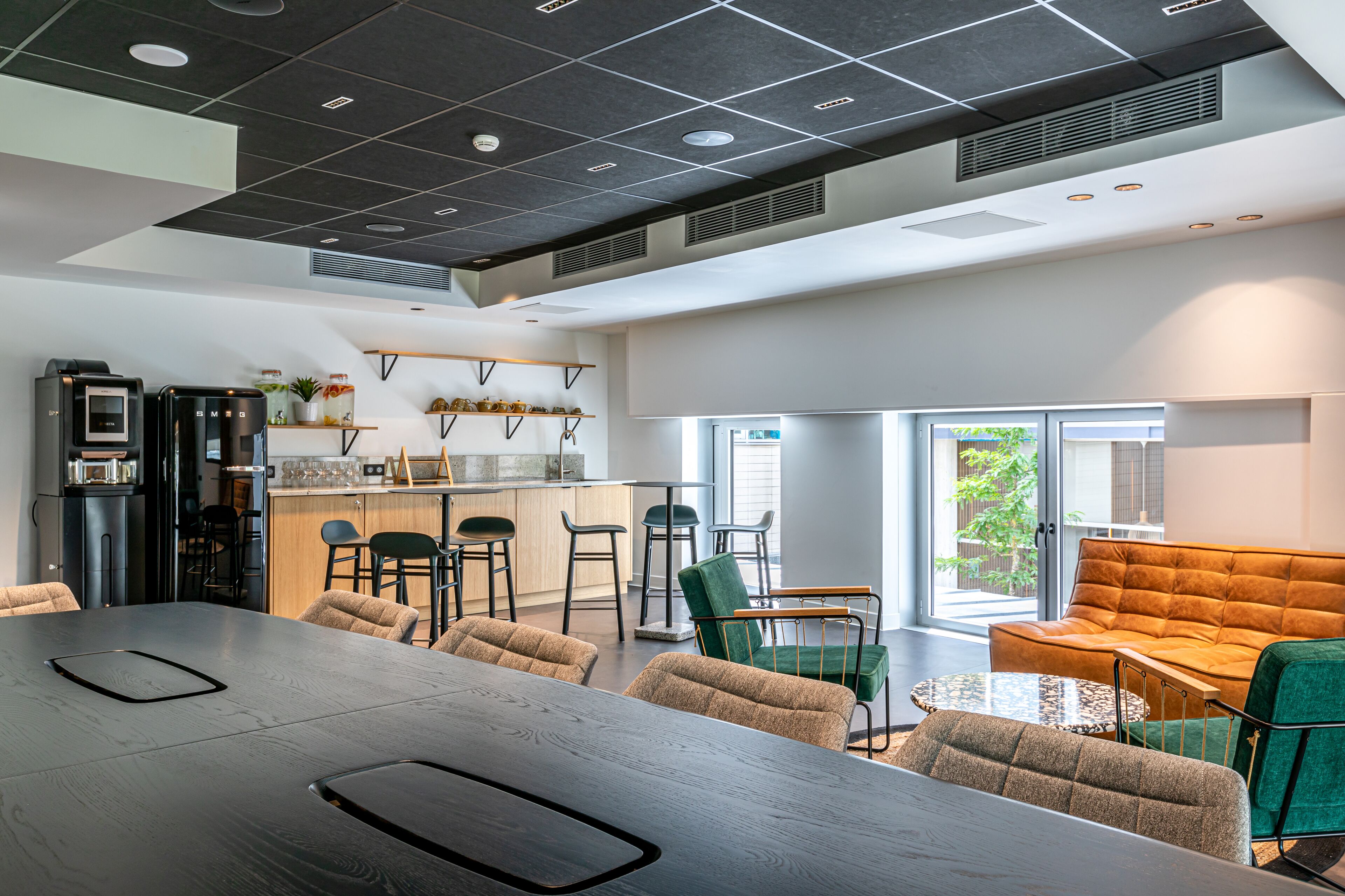 Una cocina moderna con taburetes de bar, una mesa de comedor y un sofá en un espacio luminoso con ventanas amplias.