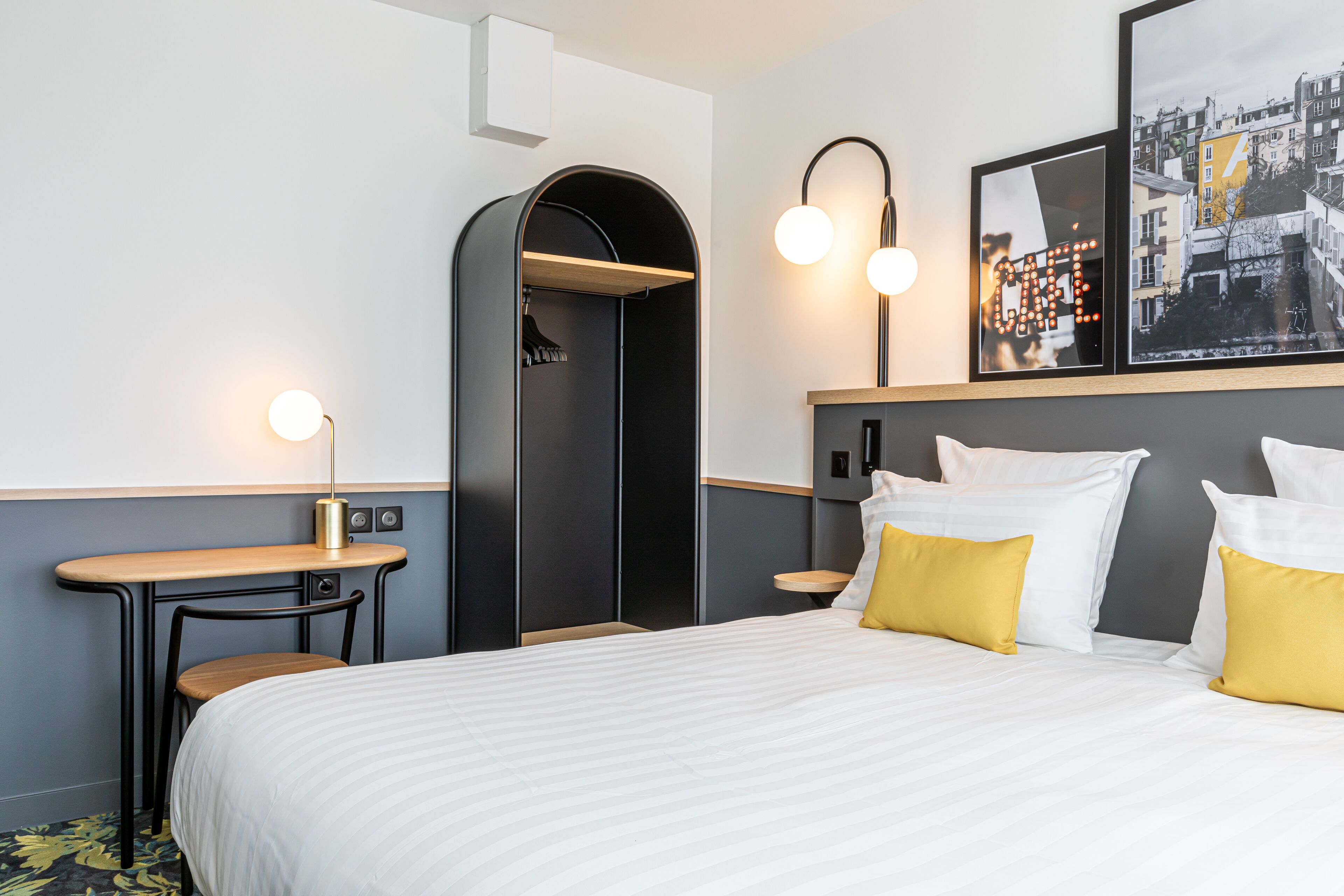 A hotel room with a bed, a desk, a chair, a wardrobe, and a framed picture on the wall.