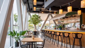 A modern bar area with a long counter, black bar stools, and a variety of bottles and glasses.